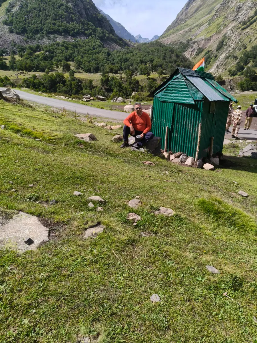 Traveller resting on a green mountain meadow beside a small hut with an Indian flag